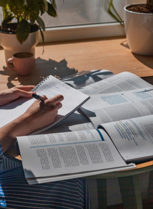 a person writing notes in front of some journals