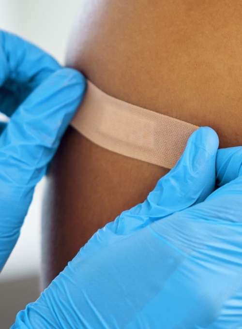 A bandaid placed on an arm by a person wearing medical gloves 