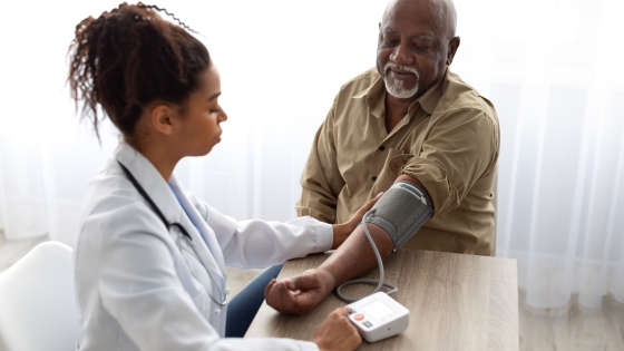 A young doctor sits at a table with an older man and measures his blood pressure.