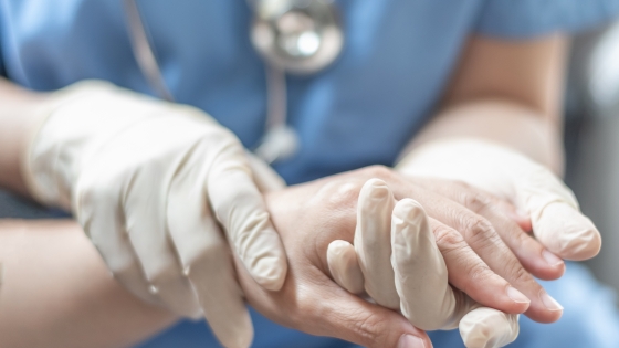 A gloved medical provider examining a patient's hand