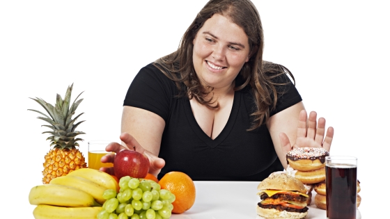 A woman sitting at a table rejects unhealthy food items and selects fruit instead.