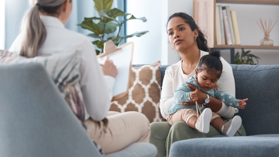 A mother holds a toddler while meeting with a clinician