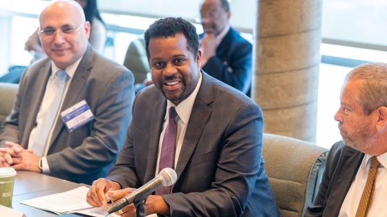 Three men sit at a table with a microphone