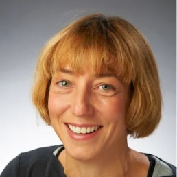 Headshot of Anna Gilmore, PhD, a woman with a light complexion, green eyes and reddish-blonde hair, wearing a smiley expression and a dark colored top