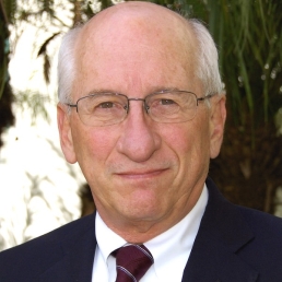 Headshot of Thomas E. Novotny, MD, a man with a light complexion, a bald head with white hair on the sides, wearing eyeglasses and a suit