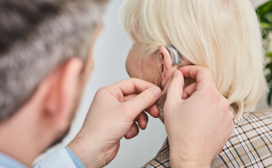 Audiologist fits hearing aid into senior woman's ear