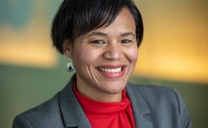 A headshot of department chair Keshia Pollack Porter. She smiles at the camera while wearing a red blouse under her grey suit jacket.