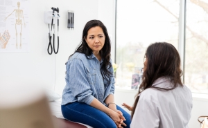 a young person sits and receives bad news from their doctor