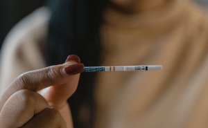 A hand holding a fentanyl test strip. Two short red lines run down the middle of the test strip.