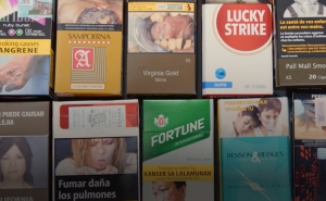 Cigarette packs from around the world lying on a grey table.