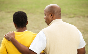 An adult man talking to a teenage boy with his arm around him