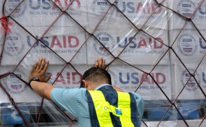 Worker pushes hands against a pallet stacked with boxes of USAID supplies