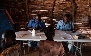 Two doctors sitting at a table consult with patients  in a clinic a camp for internally displaced persons.