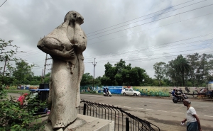 A statue of a mother holding her child with her hand over her face, against a cloudy grey sky.