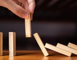 a hand picking up a domino as other dominos fall behind it