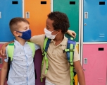 Two kids wearing masks embracing in front of school lockers