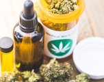 a prescription bottle with a medical marijuana label, a bottle with a dropper, and a vial, with marijuana buds in the foreground