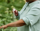 A woman spraying arms with bug repellent while on a hike.