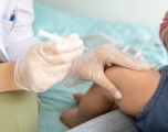 A doctor holding a syringe squeezes the thigh of a baby held by its parent