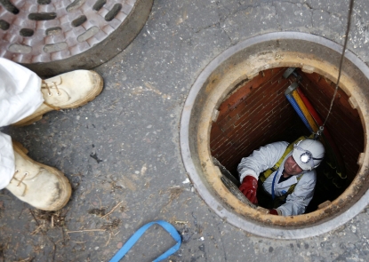 Open sewer in the middle of the street with worker climbing up while another supervises