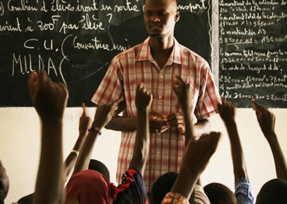 Teacher in front of classroom, with students raising their hands