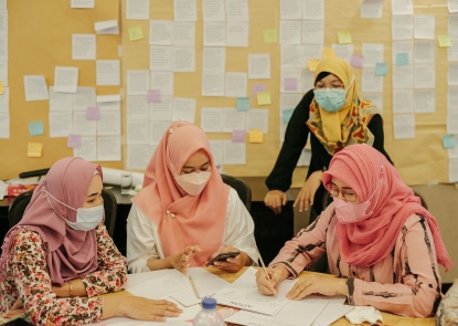 Researchers in colorful hijabs gathered around a table with lots of papers, writing and using cell phones
