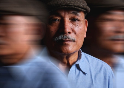 A man in focus looks intensely into the camera. A blurred version of him stands on both sides of him